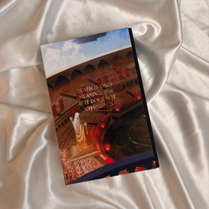 May include: A hardcover book with a colorful illustration on the cover. The image depicts a figure in a white robe, standing before a crowd. Text on the cover reads: "DEATH IS ONLY MEANINGLESS IF IT DOES NOT CHANGE US."
