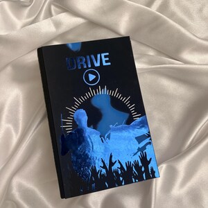 May include: A black rectangular item with the word "DRIVE" in blue metallic lettering. The item features a blue graphic of a person and hands reaching up, with a play button symbol.