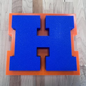 Op de afbeelding: Een witte keramische mok met een zwart handvat en de tekst "But First, Coffee" in een vetgedrukte, zwarte letter. De mok is gevuld met een donkere vloeistof, waarschijnlijk koffie, en staat op een lichtgekleurd oppervlak.