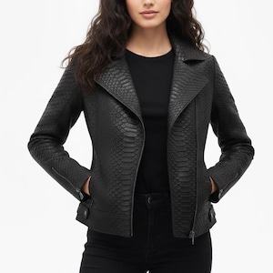 Pode incluir: Casaco de couro preto com textura de pele de cobra. O casaco tem gola entalhada, fecho de correr assimétrico e mangas com zíper. A modelo está vestida com um top preto e calças pretas.