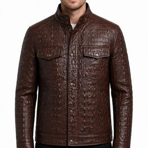 Puede incluir: Una chaqueta de color marrón oscuro con un patrón texturizado de piel de cocodrilo. La chaqueta incluye un cuello alto con botones a presión, cierre frontal de botones y dos bolsillos en el pecho con solapas. Mangas largas con puños.