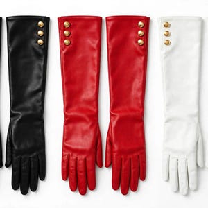 May include: Three pairs of long gloves in black, red, and white. Each pair features a smooth finish and three gold-toned metallic buttons arranged vertically along the outer wrist area. The gloves extend past the wrist, providing full hand coverage.