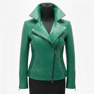 Op de afbeelding: Een groene leren jas met een textuur slangenpatroon. De jas heeft een reverskraag, een asymmetrische ritssluiting en meerdere ritszakken. De mouwen hebben ritsen bij de manchetten. De jas wordt getoond op een zwarte paspop.