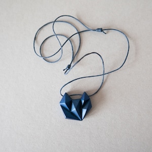 Può includere: Una collana con un ciondolo geometrico nero e un cordoncino nero.
