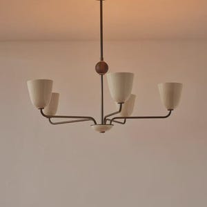 Könnte beinhalten: Ein Kronleuchter im Mid-Century-Modern-Stil mit fünf cremefarbenen, tulpenförmigen Schirmen. Die Leuchte hat ein dunkelbraunes Metallgestell und ein Holzkugeldetail. Der Kronleuchter ist an einer Deckenhalterung aufgehängt.