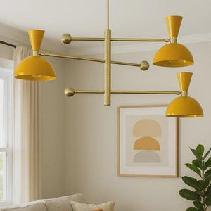Könnte beinhalten: Eine moderne, messingfarbene Hängelampe mit vier gelben, konisch geformten Lampenschirmen. Die Leuchte ist von der Decke abgehängt und hat ein geometrisches Design. Der Raum verfügt außerdem über ein Sofa in neutralen Tönen, Kunstwerke und eine Topfpflanze.