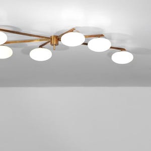 Puede incluir: Una lámpara de techo moderna con acabado en latón y múltiples luces blancas en forma de globo. La lámpara está montada en un techo blanco, creando una estética limpia y contemporánea.
