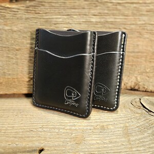 May include: Two black leather cardholders with white stitching and a debossed logo. The cardholders are rectangular with curved top edges and appear to be made of high-quality leather. The logo is a stylized "CP Leathers" design.