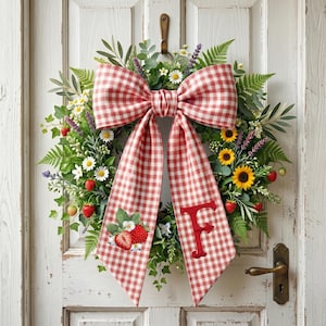 Op de afbeelding: Een decoratieve krans met een rood-witte ruitstrik en een verscheidenheid aan bloemen en groen. De krans bevat zonnebloemen, madeliefjes, aardbeien en de letter "F" op de strik.