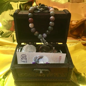 May include: A wooden treasure chest with a beaded necklace and coins inside. The chest has a metal latch and is decorated with an intricate design. The necklace is made of colourful beads and has a metal charm.