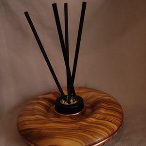 Könnte beinhalten: Dekorativer Diffusor für ätherische Öle mit Holzsockel und Kupferverkleidung. Der Sockel hat eine einzigartige, organische Form mit einem hellbraunen Holzmaserungsmuster. Schwarze Schilfrohre sind in einen schwarzen Behälter in der Mitte eingesetzt.