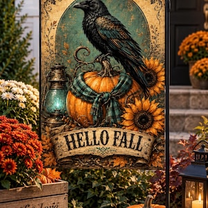 Puede incluir: Una bandera de jardín rectangular que muestra un cuervo negro posado sobre una calabaza naranja envuelta en una bufanda de cuadros verde azulado. El diseño incluye una linterna vintage, girasoles y una pancarta con el texto HELLO FALL.