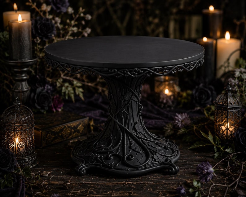 May include: A matte black cake stand featuring a circular top and a pedestal base adorned with intricate, raised vine and leaf relief patterns. The structure is uniform in color, showcasing a detailed, textured design throughout the base.