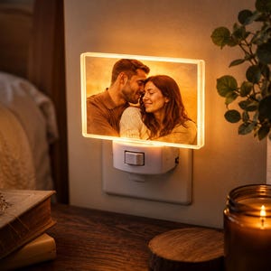 May include: A rectangular plug-in night light featuring a warm, illuminated photograph of a couple embracing. The light is mounted on a white plastic base with a manual toggle switch, emitting a soft, golden glow from the acrylic display panel.