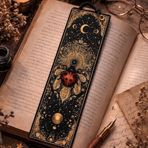 May include: A black and gold bookmark with a ladybug design, celestial elements, and a crescent moon. The bookmark is placed in an open book with a lit candle and glasses in the background. The bookmark is approximately 7 inches long.