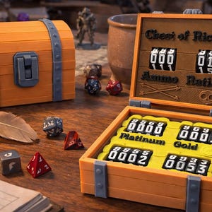 May include: Orange and gray 3D-printed treasure chest with the text "Chest of Riches" and number dials. The chest is open, revealing compartments labeled "Platinum" and "Gold" with numerical readouts. Dice and a feather are scattered around.