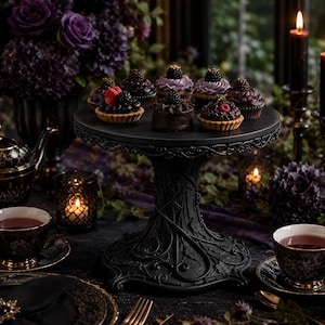 May include: A black pedestal cake stand with an intricate vine-like base design, holding an assortment of small chocolate desserts topped with fresh blackberries and raspberries, arranged on a table with black teacups and lit candles.