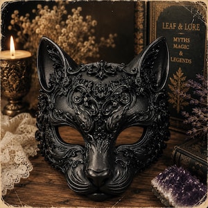 May include: A black cat mask featuring intricate, raised floral and scrollwork relief patterns across the entire surface. The mask has pointed ears, almond-shaped eye openings, and a sculpted nose and whisker area with a matte finish.