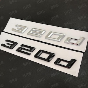 Op de afbeelding: Twee sets auto-emblemen, elk met de tekst "320d". De bovenste set is chroom, de onderste set is zwart. De emblemen staan op een witte achtergrond met herhaald "BRS" in de achtergrond.