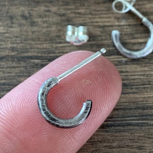 May include: A pair of silver hoop earrings with a brushed finish. The earrings are small and delicate, and they have a simple, modern design.