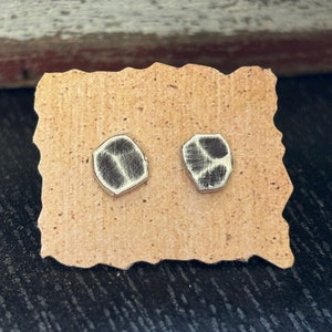 May include: A pair of silver stud earrings with a black and white geometric design. The earrings are displayed on a brown card.