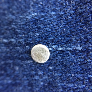 May include: Close-up of a blue denim fabric with a small, round, white button.