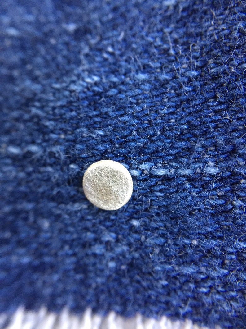 May include: Close-up of a blue denim fabric with a small, round, white button.