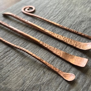May include: Set of four copper tools with hammered textures. The tools have different shapes, including a spoon, a rounded tip, and a pointed tip.