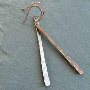May include: A pair of hammered copper earrings with a silver finish. The earrings are long and thin, with a simple wire hook.