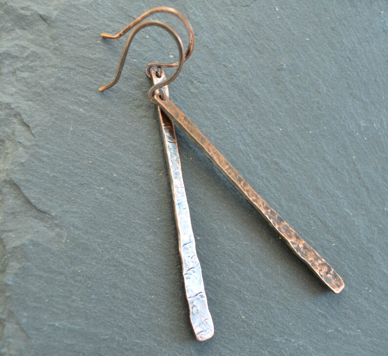 May include: A pair of hammered copper earrings with a silver finish. The earrings are long and thin, with a simple wire hook.