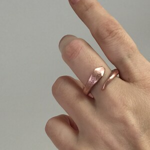Puede incluir: Un anillo de serpiente de oro rosa con un acabado texturizado. El anillo est&aacute; envuelto alrededor de un dedo.