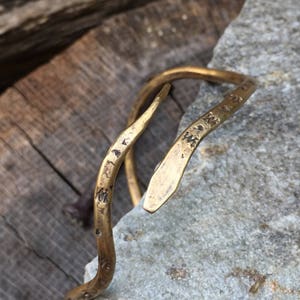 May include: A gold-toned metal bracelet with a snake-like design. The bracelet is textured and has a hammered finish.