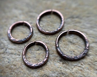 May include: Four circular metal rings with a copper-toned finish and a textured, hammered surface. Each ring features a small, visible gap at the top, indicating they are open jump rings used for jewellery making and various craft projects.