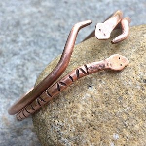 May include: A set of three copper snake bracelets. The bracelets are made of thick, rounded copper wire and are decorated with a simple, repeating pattern of small, raised dots.