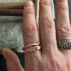 Puede incluir: Una persona lleva dos anillos en su dedo. El anillo en el dedo &iacute;ndice es una banda plateada con un dise&ntilde;o de nudo celta. El anillo en el dedo medio es una banda de cobre retorcida.