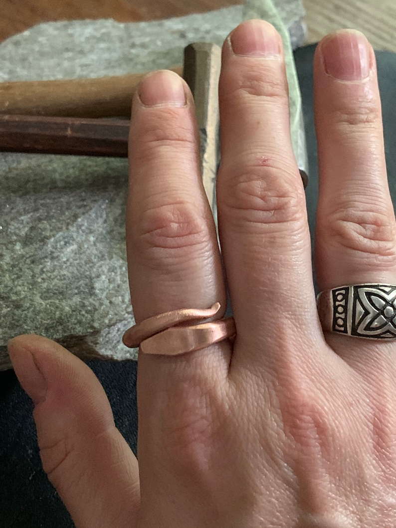 Puede incluir: Una persona lleva dos anillos en su dedo. El anillo en el dedo &iacute;ndice es una banda plateada con un dise&ntilde;o de nudo celta. El anillo en el dedo medio es una banda de cobre retorcida.