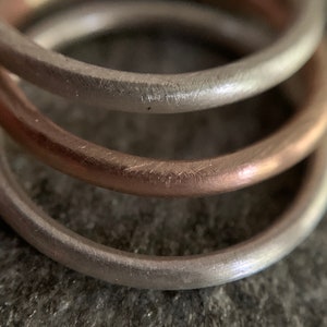 May include: Three stacked rings, one silver, one rose gold, and one silver. The rings are all smooth and have a brushed finish.
