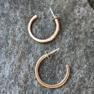May include: A pair of small, rose gold hoop earrings with a simple, minimalist design. The earrings are made of metal and have a smooth, polished finish.