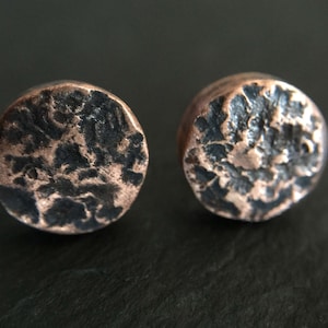May include: A pair of round, copper earrings with a hammered, textured surface. The earrings have a dark, almost black patina.