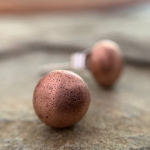 May include: A pair of copper stud earrings with a textured surface. The earrings are round and have a metallic finish.