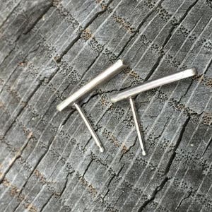 May include: A pair of silver bar earrings with a simple, minimalist design. The earrings are made of a thin, rectangular bar of metal with a post and a small back.