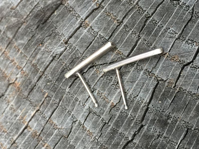 May include: A pair of silver bar earrings with a simple, minimalist design. The earrings are made of a thin, rectangular bar of metal with a post and a small back.