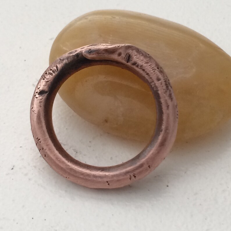 Puede incluir: Un anillo sencillo de cobre con acabado martillado. El anillo es grueso y tiene una forma redondeada.