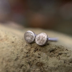 May include: A pair of small, silver stud earrings with a textured, circular design.
