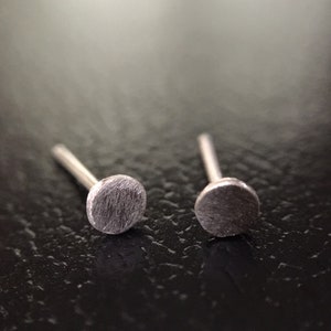 May include: A pair of silver stud earrings with a circular design. The earrings are on a dark surface.