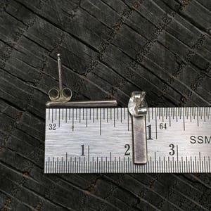 May include: A pair of silver bar earrings, measured against a ruler, showing they are approximately 2.5 cm long.