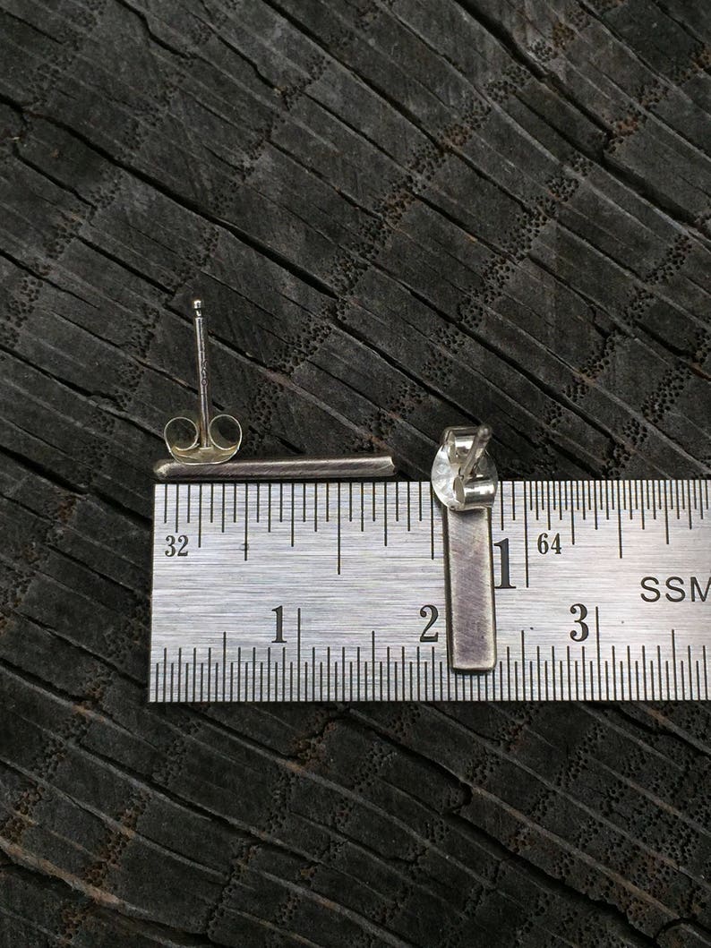 May include: A pair of silver bar earrings, measured against a ruler, showing they are approximately 2.5 cm long.
