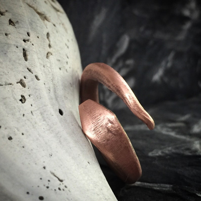 Puede incluir: Un anillo de cobre con un acabado martillado y un dise&ntilde;o &uacute;nico y retorcido.