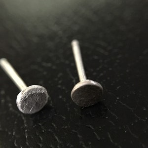 May include: Two silver stud earrings with a round, slightly textured top.