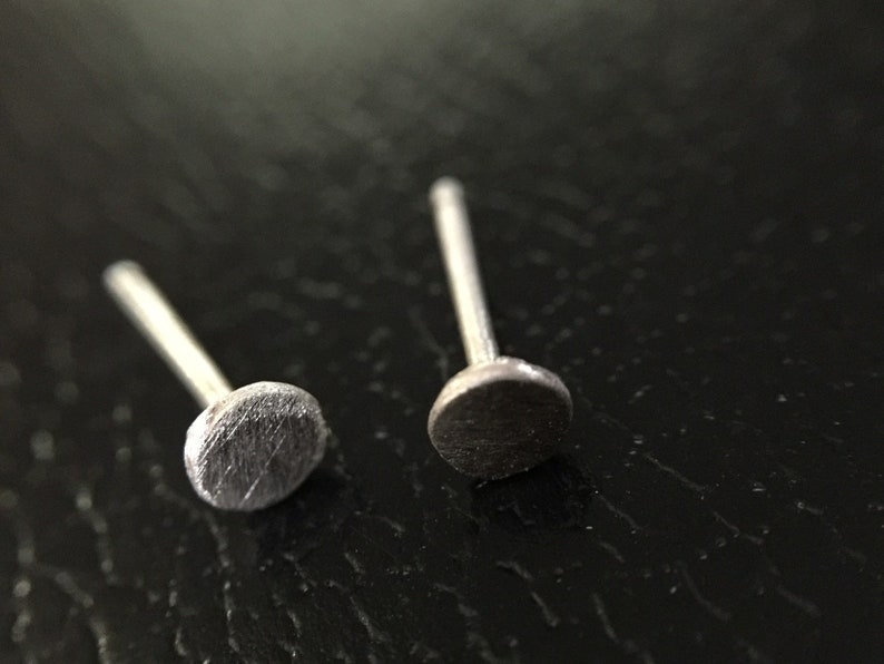 May include: Two silver stud earrings with a round, slightly textured top.